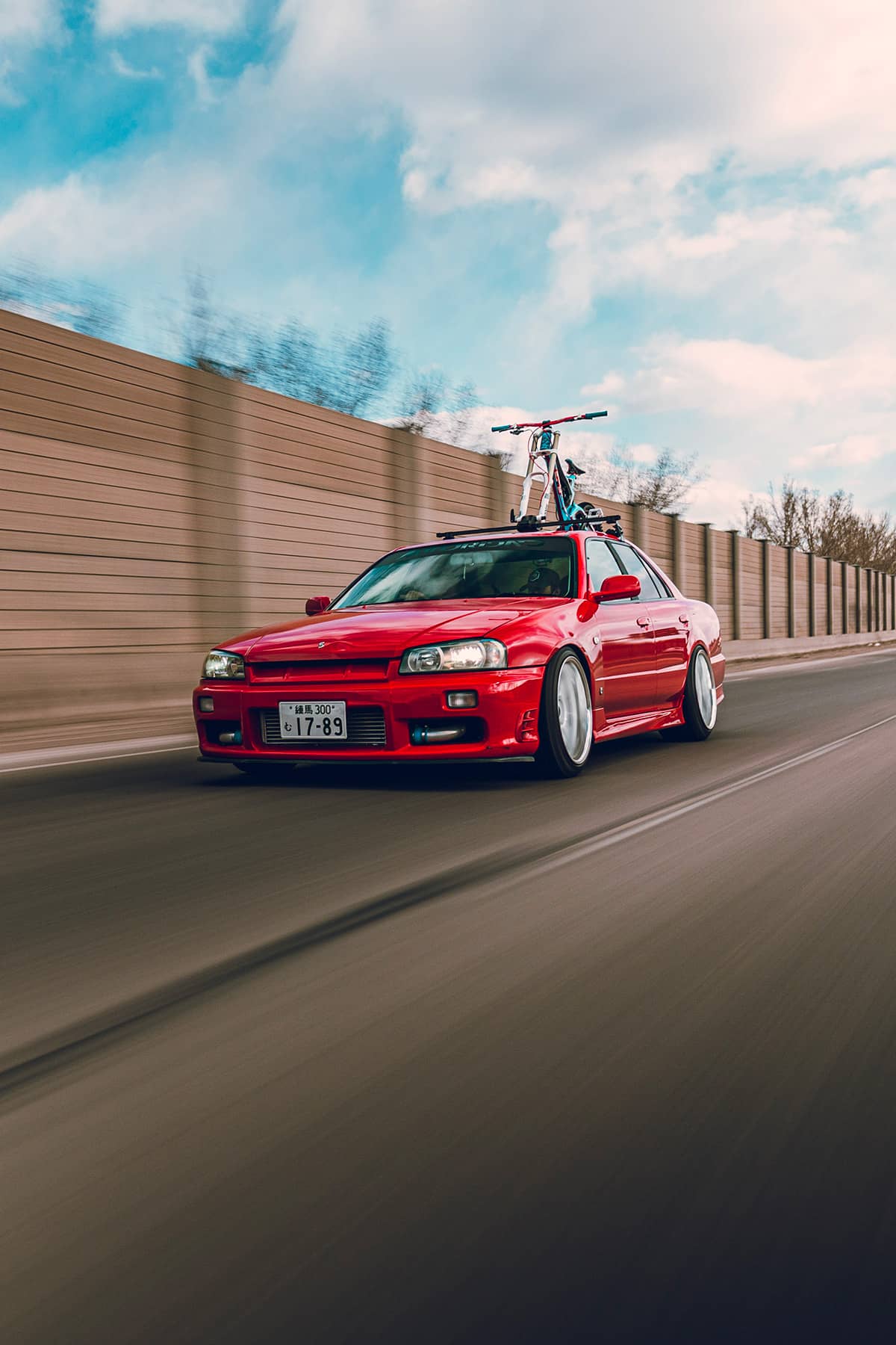 Nissan Skyline R34 sedan in red color with stance and custom wheels rolling shot